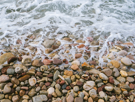 View from above at sea ocean waves with myriads of round beach stonesの写真素材
