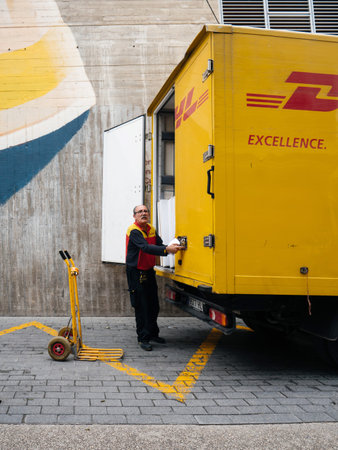 INCA, PALMA DE MALLORCA, SPAIN - MAY 8, 2018: Side view of Senior DHL postmen delivering post parcels from the yellow truck on the in central INCA town in Mallorcaのeditorial素材