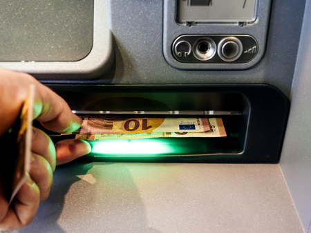 Close-up of an adult mans hand removing Euro cash money currency from slot of an automatic teller machine (ATM)の写真素材
