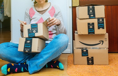 PARIS, FRANCE - JAN 13, 2018: Stack of Amazon Prime packages delivered to a home door woman unboxing one of the small boxes. Amazon is the largest internet based retailer in the United States operating worldwideのeditorial素材