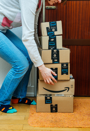 PARIS, FRANCE - JAN 13, 2018: Stack of Amazon Prime packages delivered to a home door woman trying to lift heavy boxes. Amazon is the largest internet based retailer in the United States operating worldwideのeditorial素材