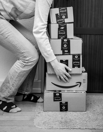 PARIS, FRANCE - JAN 13, 2018: Stack of Amazon Prime packages delivered to a home door woman trying to lift heavy boxes black and whiteのeditorial素材