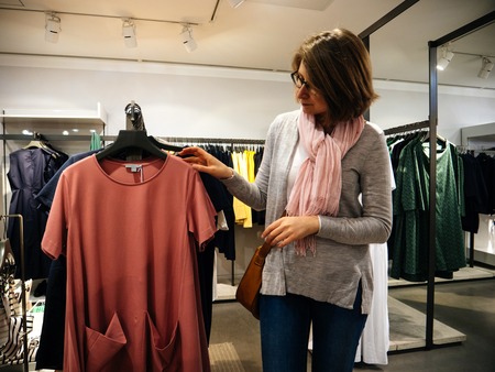Woman shopping for beautiful modern dress clothes in upscale casual fashion storeのeditorial素材