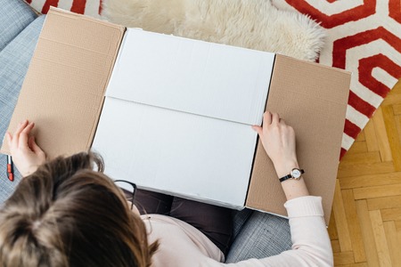 Woman unboxing cardboard box online e-commerce site delivery  - view from above in living roomの写真素材