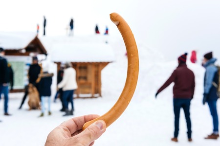 Hand point of view at long german sausage with silhouettes of people enjoying the winter snow in Mummelsee, Germanyの写真素材