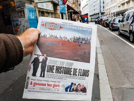 PARIS, FRANCE - JUNE 13, 2018: Man buying Liberation newspaper at press kiosk showing on cover U.S. President Donald Trump meeting North Korean leader Kim Jong-un in Singapore and Aquarius refugees boatのeditorial素材