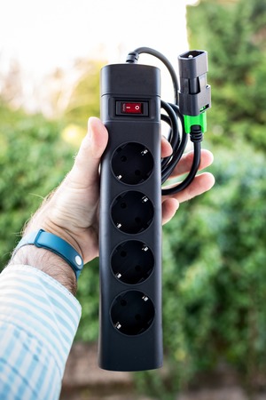 Man holding against green background power strip with four power outlets and IEC power cord to be used in back-up upsの写真素材