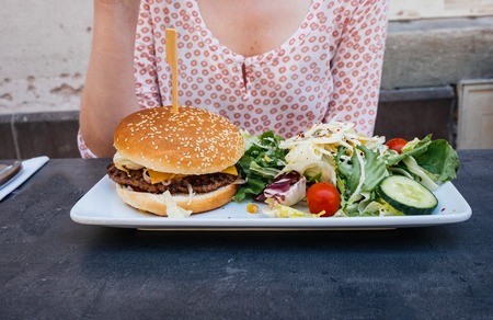 Woman eating delicious hamburger with healthy green salad on the outdoor patio of the restaurantの写真素材
