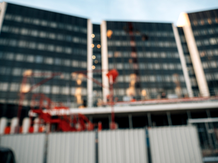 Defocused view of construction site with silhouettes of workers and cranes working in backgroundの写真素材