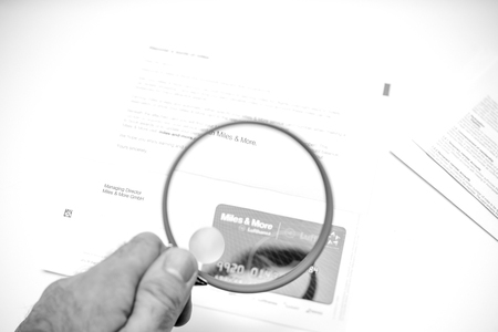 FRANKFURT, GERMANY - JAN 14, 2015: Defocused Miles and More card point card received by post from German Lufthansa airlines man using magnifying glass - black and whiteのeditorial素材