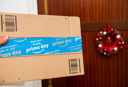 PARIS, FRANCE - JUL 12, 2108: Hand holding next to door Amazon Prime Day cardboard parcel with special blue scotch tape for the Prime Day offering a day of deals, discounts, and unabashed shoppingのeditorial素材