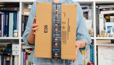 PARIS, FRANCE - JUL 4, 2018: Woman holding new presentation of Amazon Prime package delivered preparing to do the unboxing, proud Amazon Prime client with library in backgroundのeditorial素材