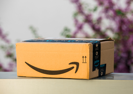 PARIS, FRANCE - APR 19, 2018: Delivered Amazon Cardboard box left outdoor the house by courier with large Amazon Smile  against defocused tree backgroundのeditorial素材