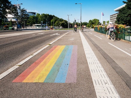 STRASBOURG, FRANCE - JUL 18, 2018: Gay pride LGBT flag in front of the European Court of Human Rights building with buses, cars and pedestrians in the eveningのeditorial素材