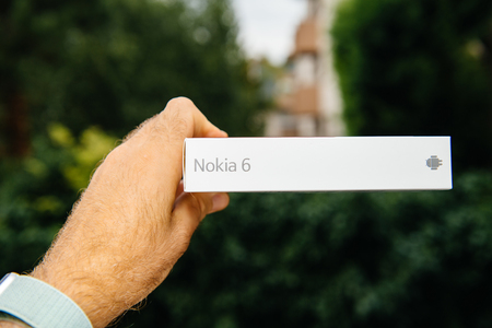 PARIS, FRANCE - AUG 1, 2018: Man hand holding new box of Nokia 6 Android smartphone against green nature background - side view of the boxのeditorial素材
