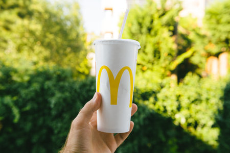 PARIS, FRANCE - JUL 27, 2018: Man holding outdoor against green background a cup of McDonalds Cola...