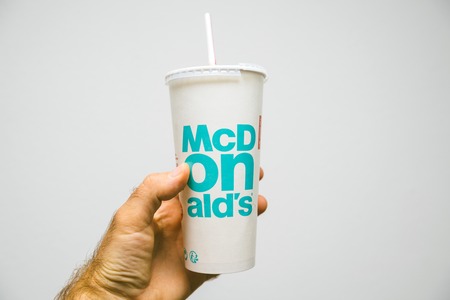 PARIS, FRANCE - JUL 27, 2018: Man holding inside restaurant against white background a cup of McDonalds Cola with plastic straw with blue textのeditorial素材