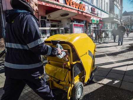 HAMBURG, GERMANY - MAR 20, 2018: Man in uniform pushing Deutsche Bank DHL German post yellow carriage with mail walking down streetのeditorial素材