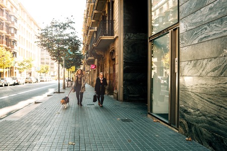 BARCELONA, SPAIN - OCT 11, 2017: Adult women with dog on leash walking down street in leisure having calm stroll, Barcelonaのeditorial素材