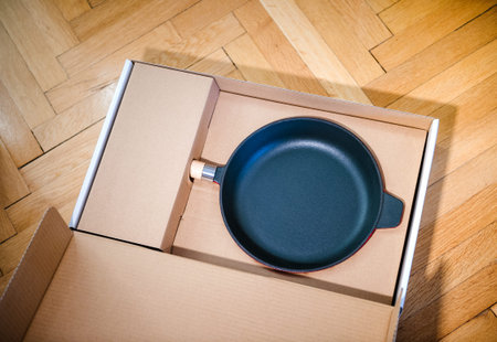 Unboxing of professional black fry pan on kitchen parquet wooden background - view from above,...