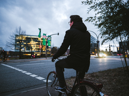 HAMBURG, GERMANY - MAR 21, 2018: Anonymous man on bicycle standing on roadside waiting for green light in dusk timeのeditorial素材