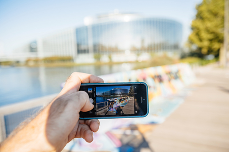 STRASBOURG, FRANCE - SEP 12, 2018: Man taking photo with iphone smartphone telephone with SaveYourInternet placard poster in front of south facade of European Parliamentのeditorial素材