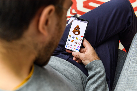 LONDON, UK - SEP 21, 2018: Man using the new pile of poo AR Memoji emoji face on Apple iPhone Xs with the immense OLED retina display and a12 bionic chipのeditorial素材