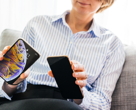 PARIS, FRANCE - SEP 27, 2018: Elegant French woman testing and comparing the newest latest iPhone Xs and Xs Max smartphone telephone from Apple Computers testing the screen sizeのeditorial素材