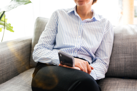 PARIS, FRANCE - SEP 27, 2018: Elegant French woman holding silicone case for the newest latest iPhone Xs and Xs Max smartphone telephone from Apple Computers on office living room sofaのeditorial素材