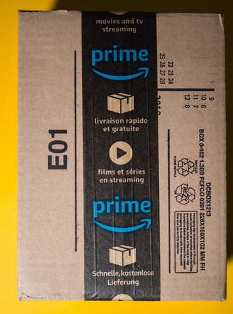 PARIS, FRANCE - SEP 28, 2018: New Amazon Cardboard box against yellow background with seal scotch tape featuring prime video and one day deliveryのeditorial素材