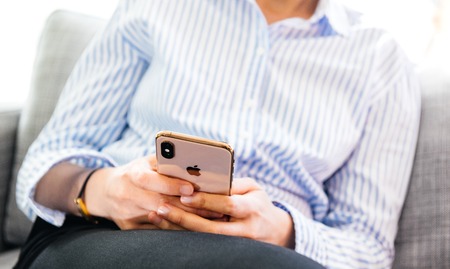 PARIS, FRANCE - SEP 27, 2018: latest iPhone Xs and Xs Max smartphone telephone from Apple Computers in woman hands while using the gold phone relaxes on office living room sofaのeditorial素材