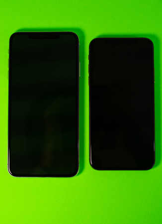 PARIS, FRANCE - SEP 27, 2018: Two Apple Computers iPhone Xs and Xs Max as hero object on bright glamorous modern neon pop green background - smartphone telephone with OLED display with black display screenのeditorial素材