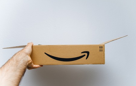 PARIS, FRANCE - AUG 11, 2018: Man holding against white background freshly unboxed Amazon Prime cardboard boxのeditorial素材