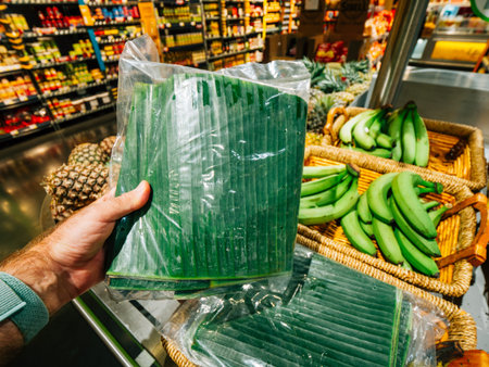 Male hand shopping fresh banana leaves in large fruits and vegetables supermarket store - choosing the bio organic fruitの写真素材