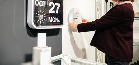 Wide image of elegant French woman shopping for clocks in furniture store - diverse types of wall clocks modern and vintageの写真素材