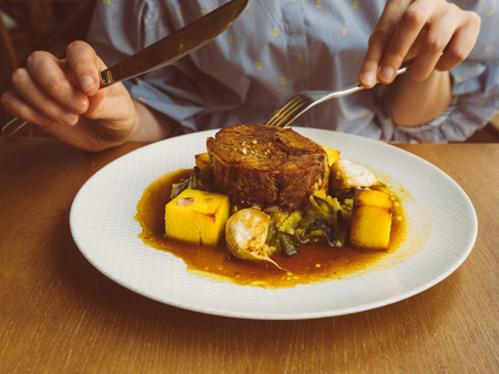 French woman eating in restaurant delicious lamb meat with sauce and polenta and delicious baked garlic - vintage filterの写真素材