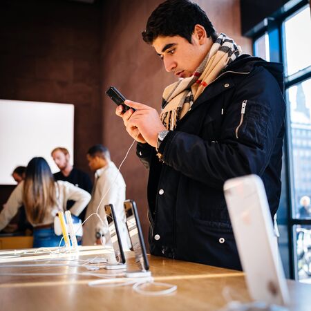PARIS, FRANCE - OCT 26, 2018: Side view of young male customer admiring the latest iPhone XR smartphone in Apple Store Computers during the launch day - square imageのeditorial素材