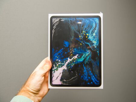 PARIS, FRANCE - NOV 14, 2018: Man holding POV at the front packaging the latest iPad Pro by Apple Computers tablet retail box against gray backgroundのeditorial素材