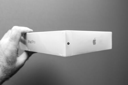 PARIS, FRANCE - NOV 14, 2018: Man holding POV the latest iPad Pro by Apple Computers tablet retail box against gray background - admiring the side view of the box with the open plastic box accessのeditorial素材