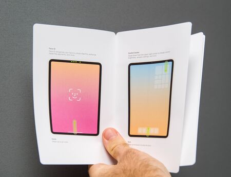 PARIS, FRANCE - NOV 14, 2018: Man hand holding unboxing unpacking of new iPad Pro by Apple Computers tablet holding the instruction manual paper in front against gray backgroundのeditorial素材