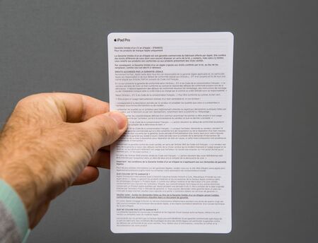 PARIS, FRANCE - NOV 14, 2018: Man hand holding unboxing unpacking of new iPad Pro by Apple Computers tablet holding the warranty manual paper in front against gray backgroundのeditorial素材