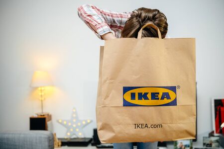 PARIS, FRANCE - DEC 2, 2018: Casual dressed woman holding big paper IKEA bag full with merchandise from the famous swedish furniture retailer - searching inside the bagのeditorial素材