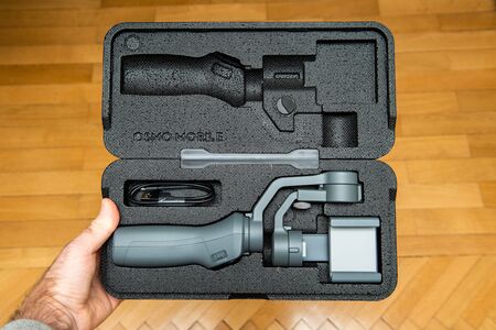PARIS, FRANCE - NOV 22, 2018: Man unboxing new DJI Osmo Mobile 2 Smartphone Gimbal manufactured by the SZ DJI Technology Co., Ltd company holding the foam packaging above the wooden floorのeditorial素材