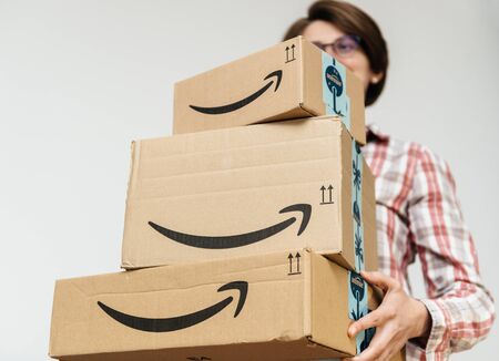 PARIS, FRANCE - DEC 2, 2018: Casual dressed woman holding three unopened sealed heavy Amazon Prime parcel cardboard box stack one above another ready for winter holidays gifts shoppingのeditorial素材