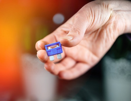 Woman hand holding blue amp rated car fuses before inserting them fuse box closeup shotの写真素材