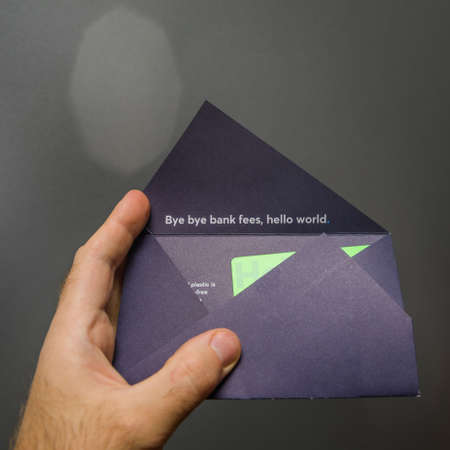 Paris, France - Mar 14, 2018: Man hand unboxing new TransferWise Borderless Account multi-currencies Mastercard debit card with slogan bye bye bank fees, hello worldのeditorial素材
