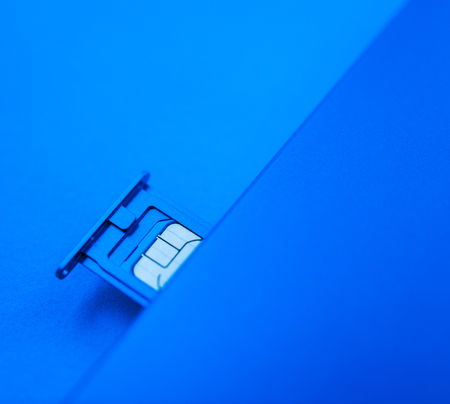 Micro SIM card subscriber identity module inside new smartphone telephone mobile device against blue backgroundの写真素材