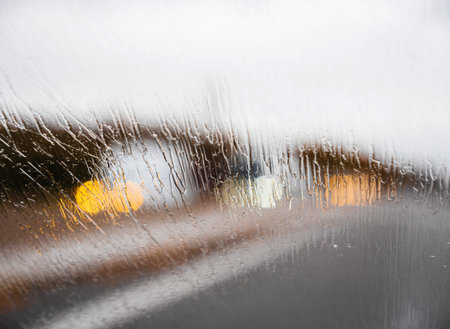 Multiple water drops on windshield on a fast driving car on highway with green leaves on the side of...