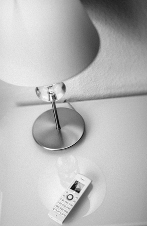 Modern white cordless phone on white living room office interior table next to a desk lamp - view from above of cozy interior decoration - black and whiteの写真素材