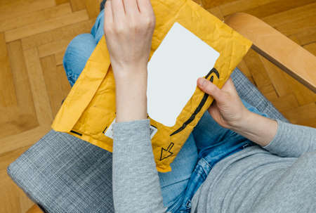 PARIS, FRANCE - NOV 4, 2017: Woman unboxing on the living room armchair the Amazon Prime cardboard envelope with a giftのeditorial素材